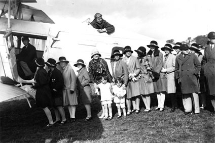 Sir Alan Cobham in the cockpit of his de Havilland D.H.61 biplane with a line of children waiting for their free flight