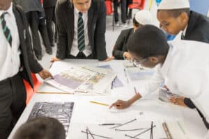 A group of school students gathered round documents on a table.