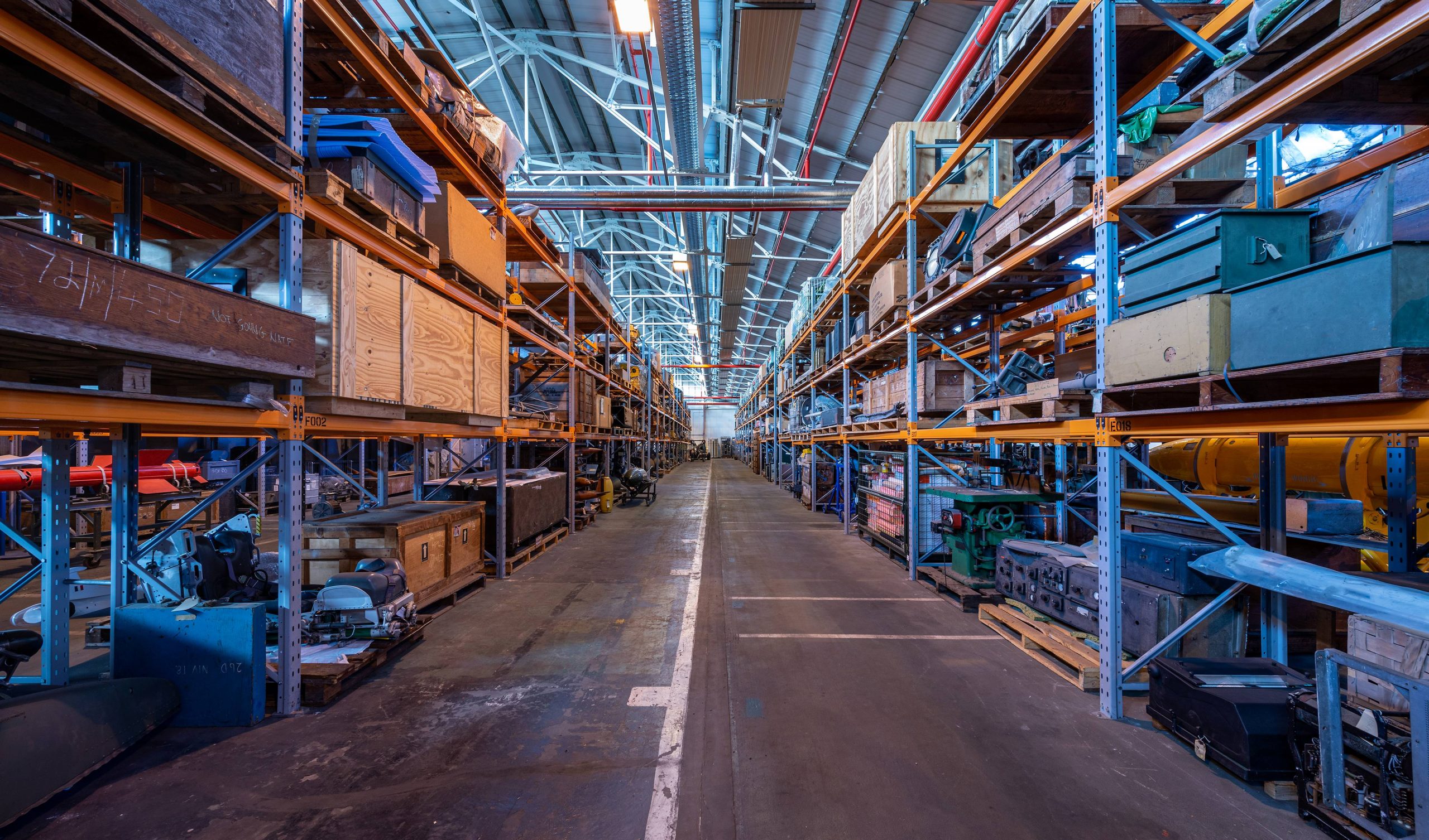 The image shows a warehouse with several containers on shelves. The building appears to be made of steel and is used for storage