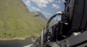 Cockpit view from inside a Typhoon flying through a mountain valley, with another Typhoon visible in the distance under a partly cloudy sky.