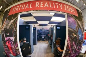 Several people sit in partitioned VR booths inside the RAF Museum’s “Virtual Reality Zone,” surrounded by vibrant graphics of aircraft controls and flight imagery.